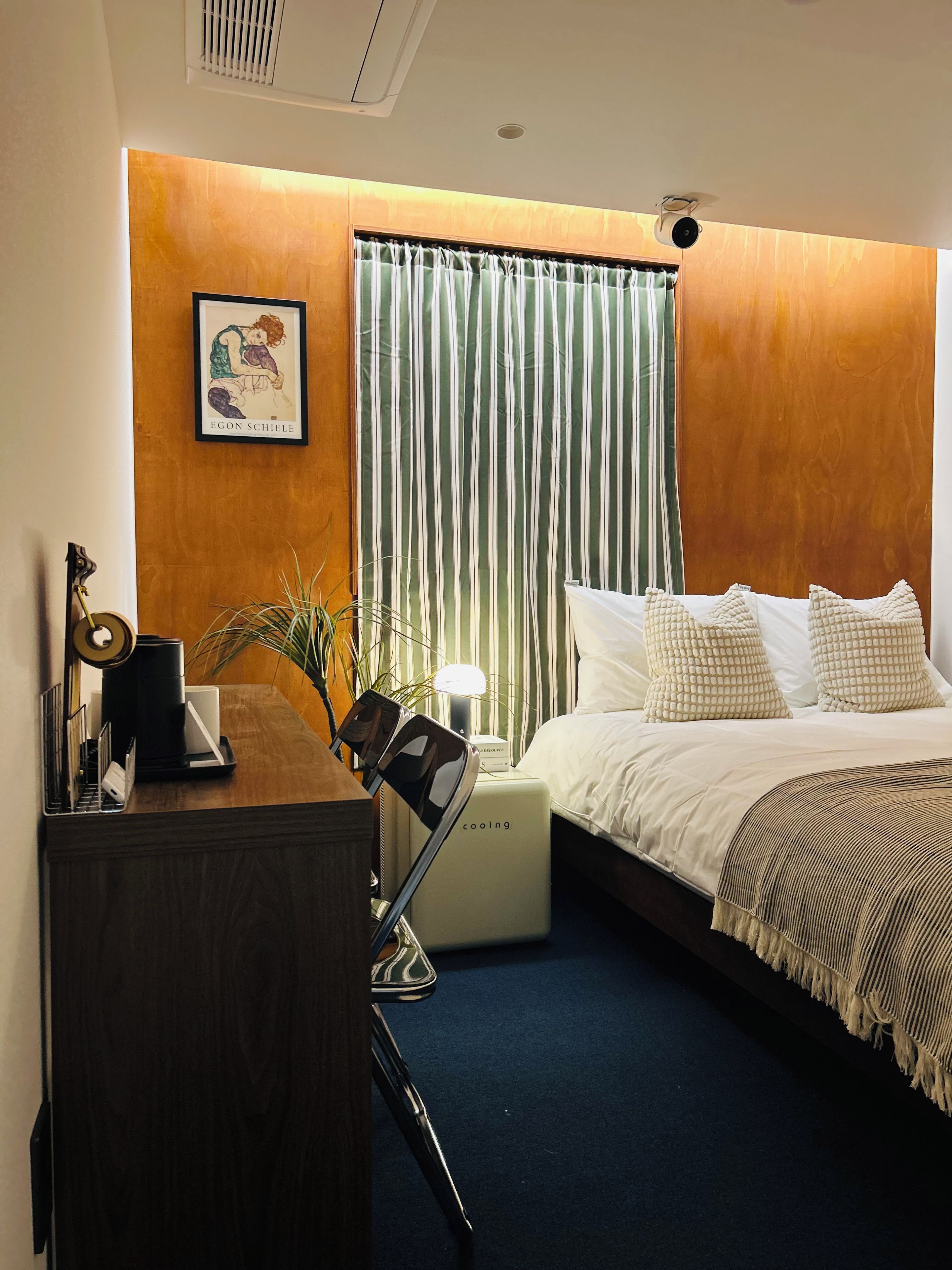 Ein Hotelzimmer mit Bett, Schreibtisch mit Lampe, einem gerahmten Bild an der Wand und einem Fenster mit Vorhängen.