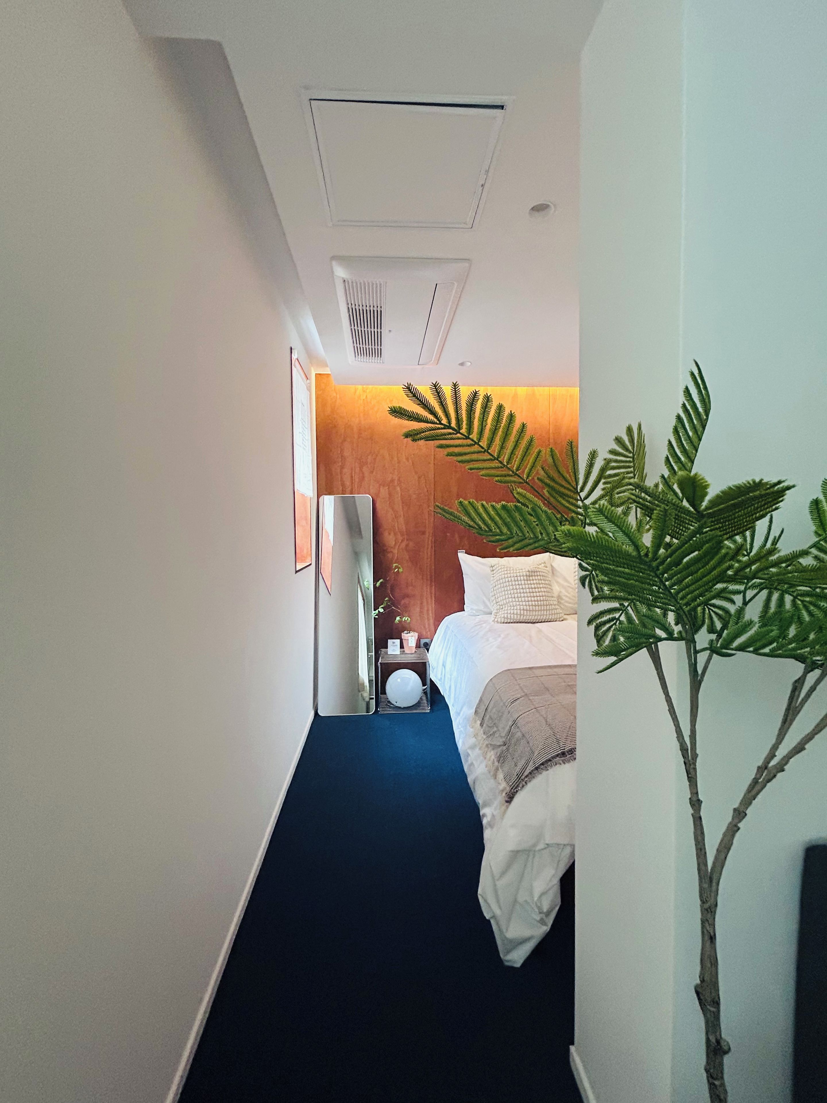 A hotel room with a bed, bedside table, and a mirror.