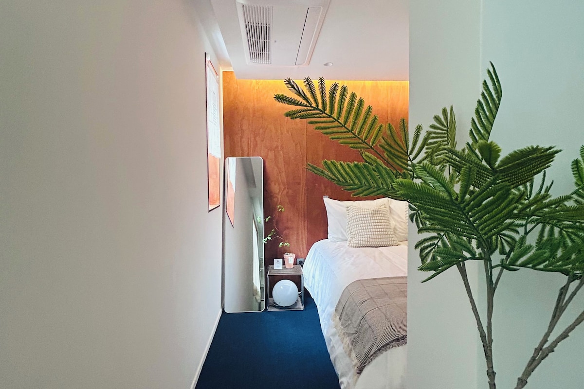 A hotel room with a bed, bedside table, and a mirror.