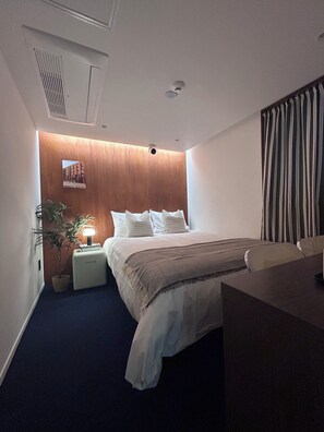A hotel room with a bed, bedside table, lamp, and a potted plant.