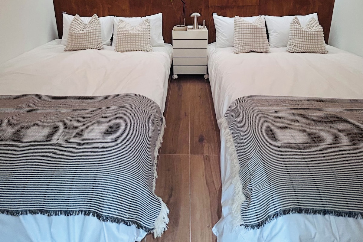 A hotel room with two beds, a nightstand, and a wooden headboard.
