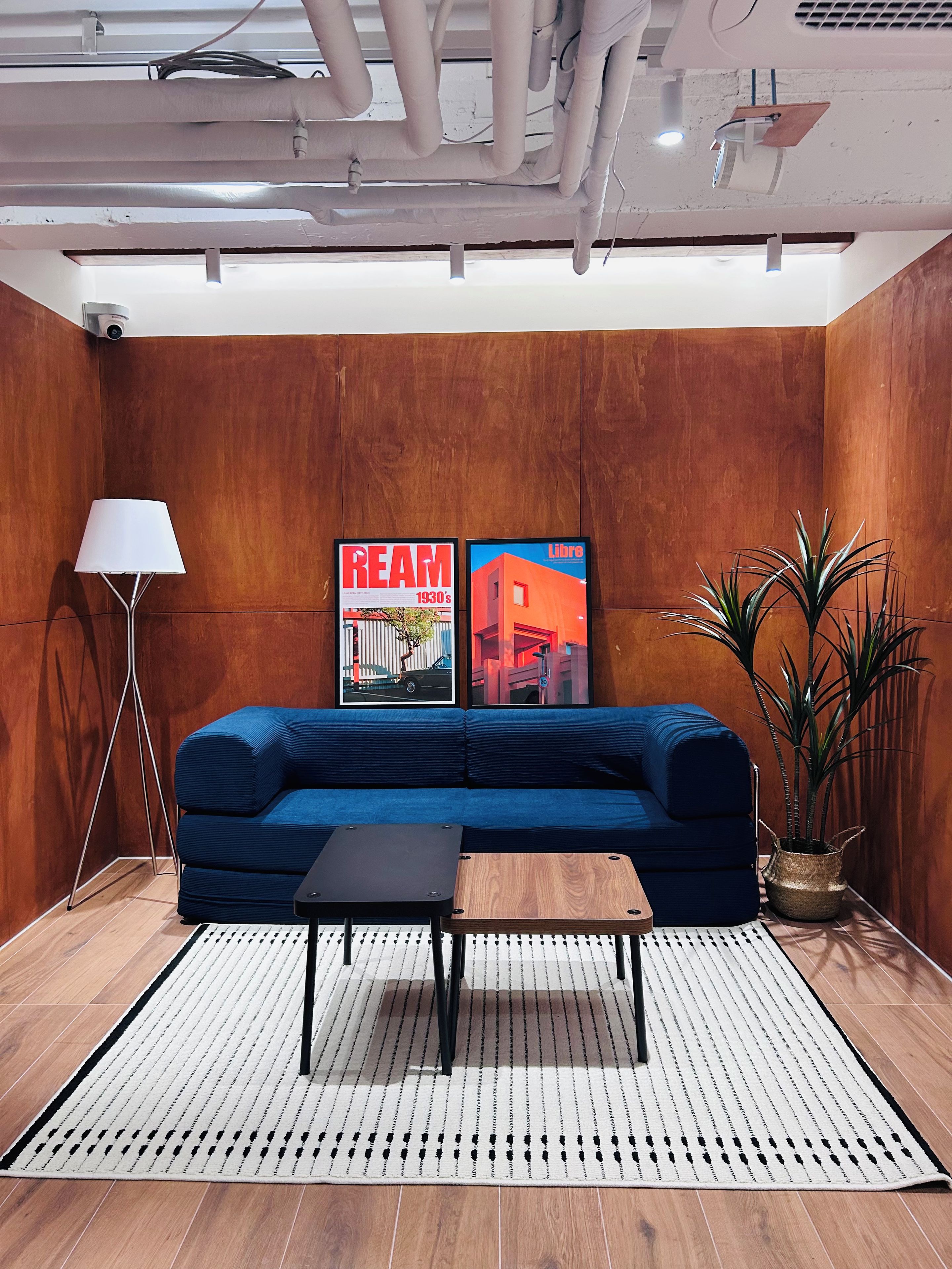 A modern living room with a blue sofa, a small wooden coffee table, a floor lamp, and two framed pictures on the wall.
