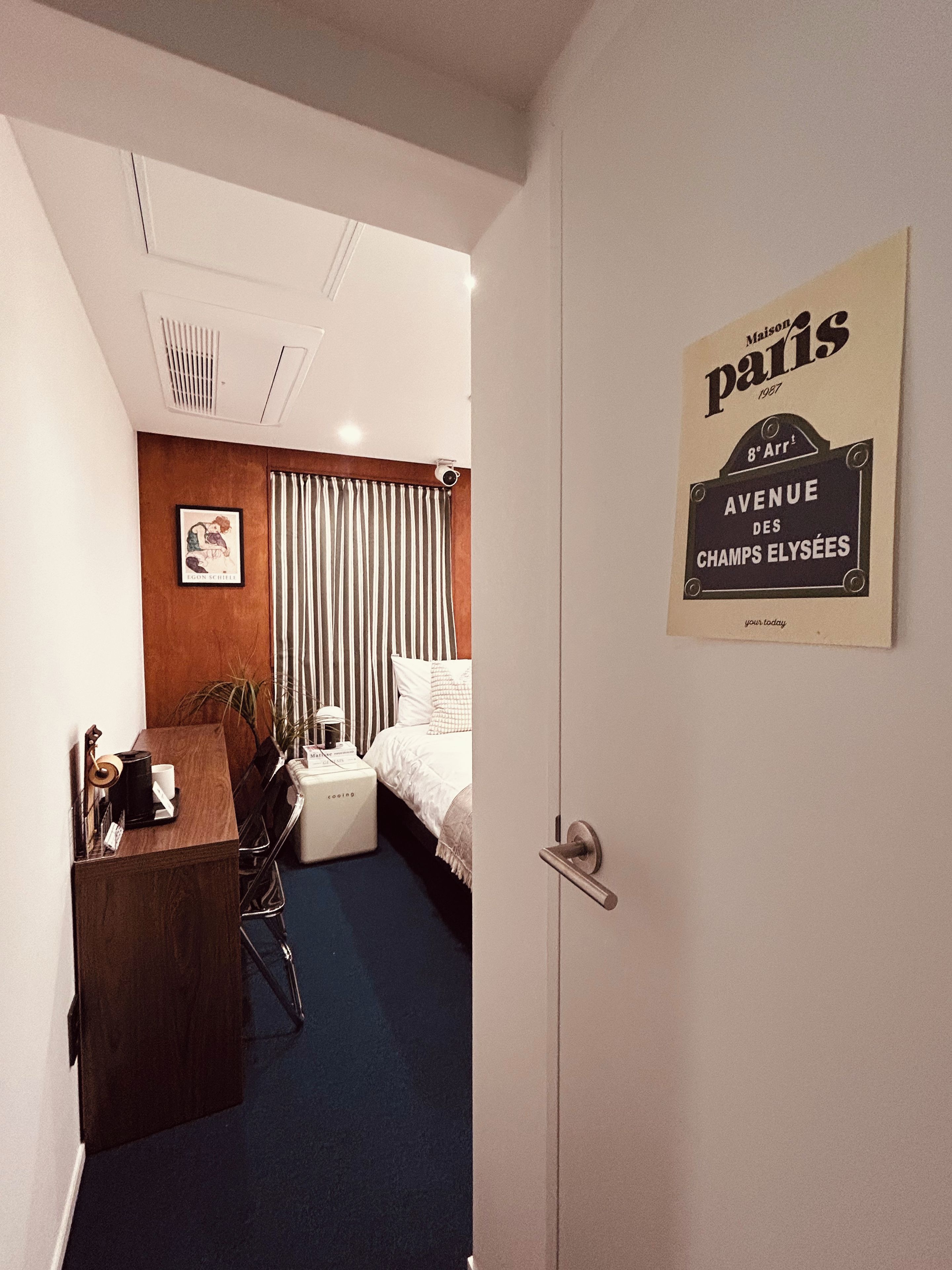 Habitación de hotel con cama, escritorio, silla, máquina de café y un letrero que indica la ubicación como '8º arrondissement, Avenida de los Campos Elíseos, París'.