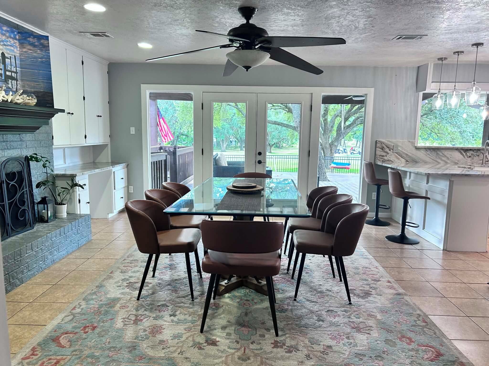 A dining area with a glass table, four chairs, a ceiling fan, and a view of the outdoors through large sliding doors.