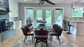 A dining area with a glass table, four chairs, a ceiling fan, and a view of the outdoors through large sliding doors.