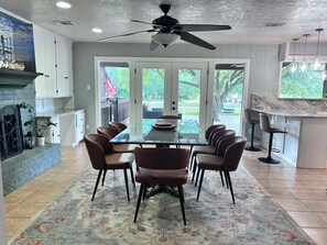 A dining area with a glass table, four chairs, a ceiling fan, and a view of the outdoors through large sliding doors.