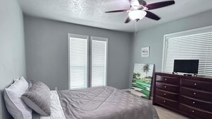 Quarto com cama, cômoda, ventilador de teto e um quadro na parede.