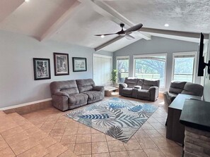 A spacious living room with a ceiling fan, large windows, and a grey sofa.