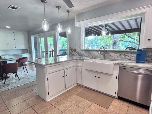 A kitchen with white cabinets, a marble countertop, a stainless steel sink, and pendant lights.