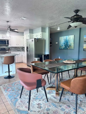 A modern kitchen with white cabinets, a stainless steel refrigerator, and a microwave. There is a dining area with a glass table and brown chairs. - Tranquil 3-bedroom house with AC in charming Bryan (Bryan)