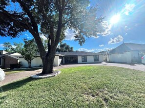 A residential area with a large tree in the foreground, a house with a sloped roof, and a clear sky.