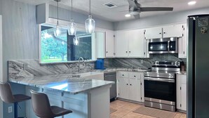 Uma cozinha com bancada de mármore, eletrodomésticos de aço inoxidável e iluminação pendente.