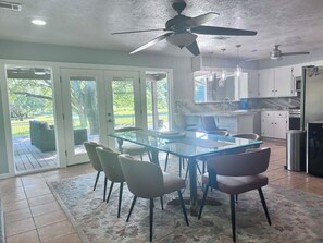 A modern kitchen with a glass dining table and chairs, a ceiling fan, and a view of the outdoors.