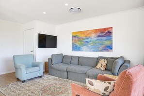 A living room with a grey sofa, a blue armchair, and a colorful abstract painting on the wall. - 14 Seashapes - Coastal Comfort With Open Spaces & Beach Glimpses (Maroochydore)