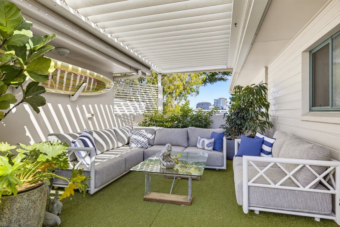 Een terras buiten met een modulaire bank, een glazen salontafel en potplanten.
