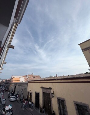 Vista de una calle con edificios, cielo despejado y algunas personas caminando.