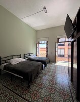 Una habitación con dos camas, televisión y balcón con vistas a edificios.