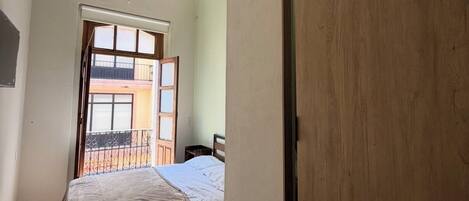 Um quarto com cama, guarda-roupa de madeira, janela com vista e luminária no teto.