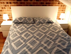 A bed with a geometric patterned bedspread, two bedside lamps, and a brick wall in the background.