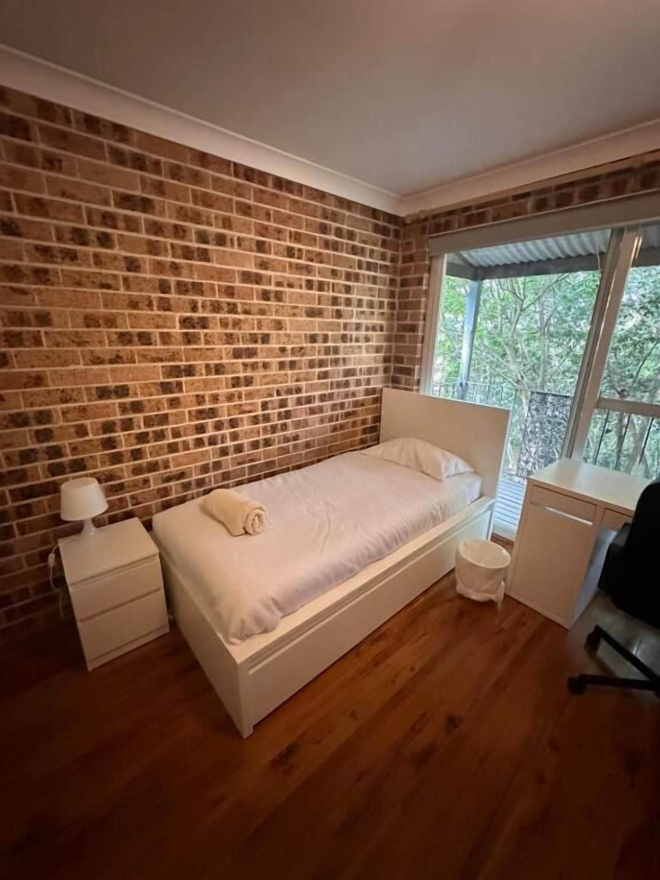 Ein Schlafzimmer mit Backsteinwand, einem Bett, einem Schreibtisch und einem Fenster.