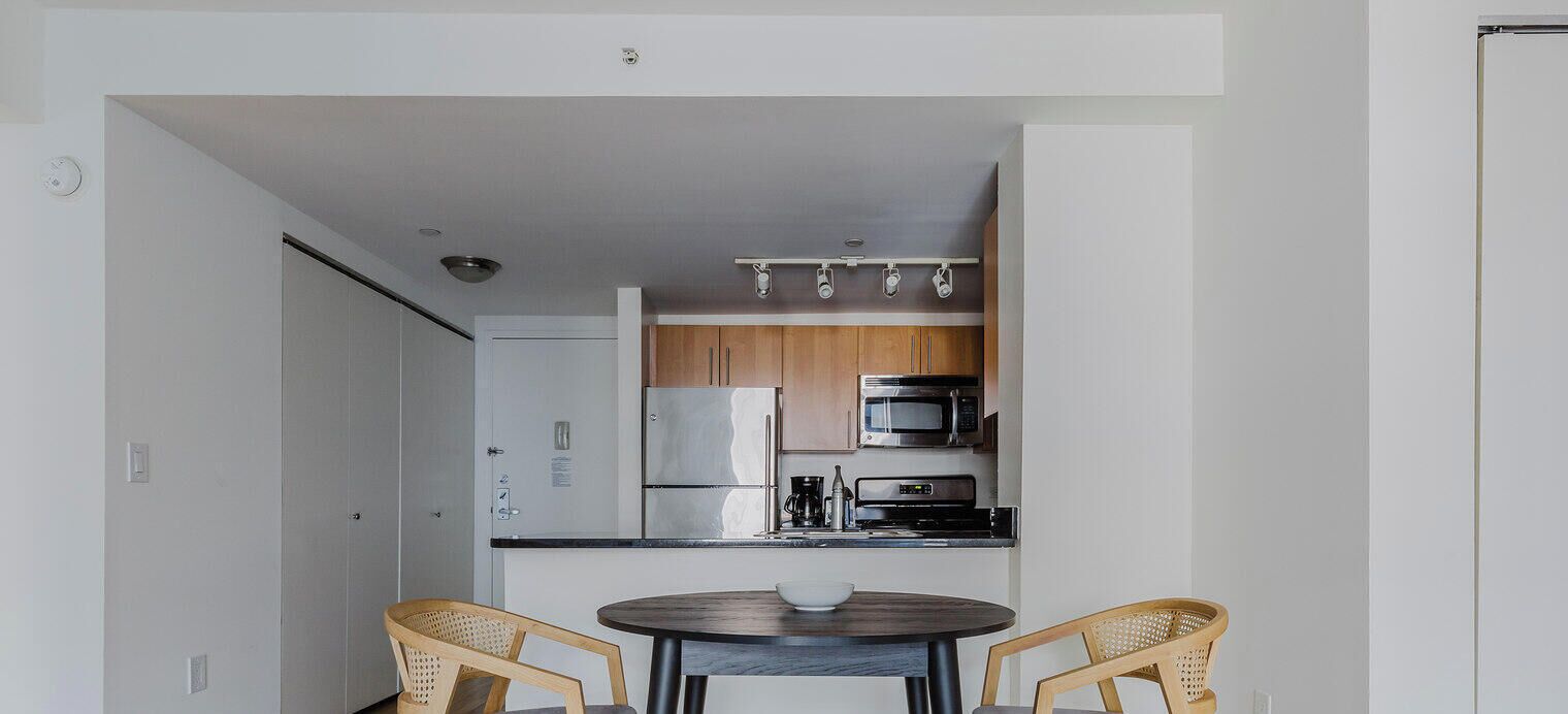 A compact kitchen with a refrigerator, microwave, and coffee maker. There is a round table with two chairs in the foreground.