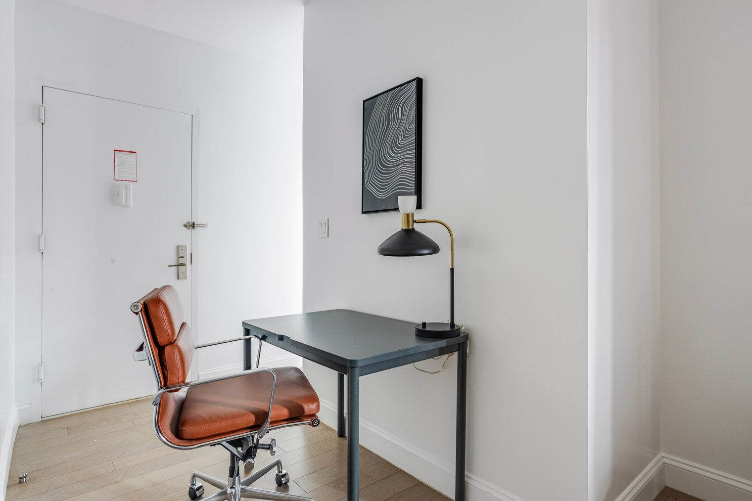 A small office space with a desk, chair, and a single wall-mounted lamp.
