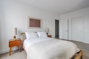 A bedroom with a bed, two bedside tables with lamps, a framed abstract artwork, and a set of double doors. - Blueground | Bloomingdale, gym, nr Riverside Park (New York)