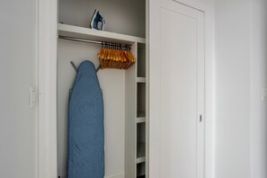 A closet with a hanging rack, an ironing board, and a shelf with a blue iron. - Blueground | Bloomingdale, gym, nr Riverside Park (New York)