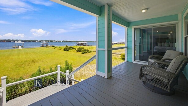 A covered porch with a view of a grassy area and water, a seating area with wicker chairs, and a sign indicating 'KINGSWOOD RENTAL'. - Little Lagoon Waterfront • Private Pier • West Beach •  Dockside Oasis by Kaiser (Gulf Shores)