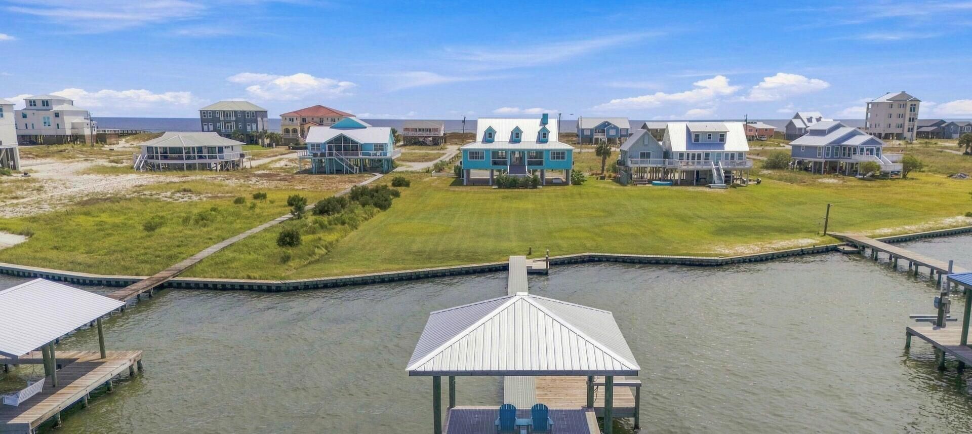 Una zona residencial costera con casas, un muelle y un campo cubierto de hierba.
