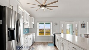 A modern kitchen with stainless steel appliances, white cabinetry, a large window, and a ceiling fan. - Little Lagoon Waterfront • Private Pier • West Beach •  Dockside Oasis by Kaiser (Gulf Shores)