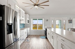A modern kitchen with stainless steel appliances, white cabinetry, a large window, and a ceiling fan. - Little Lagoon Waterfront • Private Pier • West Beach •  Dockside Oasis by Kaiser (Gulf Shores)