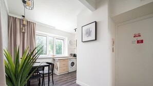 Une cuisine moderne équipée d’un lave-linge, d’un coin repas avec une table et des chaises, et d’une grande fenêtre avec des rideaux.