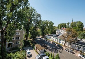 Una strada residenziale con auto parcheggiate, alberi e edifici, tra cui una chiesa con campanile.
