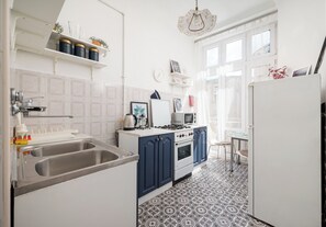 A kitchen with a double sink, stove, and refrigerator. There are shelves above the sink and a clock on the wall. - Hoża Artistic Charm Studio (Warszawa)