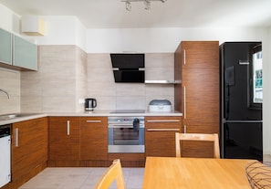A compact kitchen with wooden cabinets, a built-in oven, and a black refrigerator. - Metro Wilanowska Classic Apartment (Warszawa)