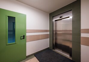 Un couloir avec une porte verte, un ascenseur fixé au mur et un paillasson.