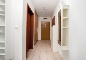 Un couloir avec des portes en bois, des étagères blanches et un sol carrelé.