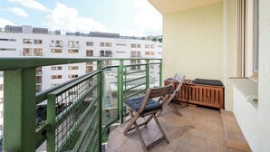 Ein Balkon mit Holzstuhl und kleinem Tisch, mit Blick auf ein Wohngebiet mit mehreren Gebäuden.