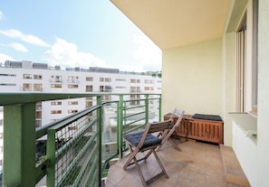 Ein Balkon mit Holzstuhl und kleinem Tisch, mit Blick auf ein Wohngebiet mit mehreren Gebäuden.
