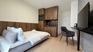 A modern hotel room with a bed, a desk with a television, a chair, and a kitchenette. - Madalińskiego Modern Studio 8B (Wrocław)