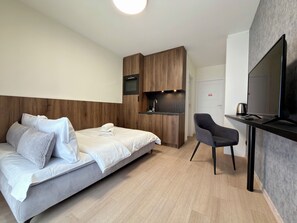 Ein modernes Hotelzimmer mit einem Bett, einem Schreibtisch mit Fernseher, einem Sessel und einer Küchenzeile.