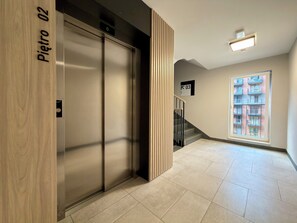 An interior corridor with a wooden door labeled 'Pietro 02,' a staircase, and a window with a view of a building. - Madalińskiego Modern Studio 8A (Wrocław)