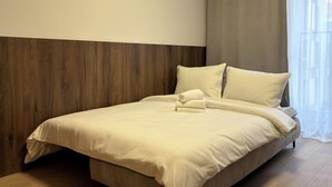 Ein ordentlich bezogenes Bett mit einem gefalteten Handtuch, einem hölzernen Kopfteil und einem Fenster mit durchsichtigen Vorhängen.