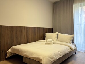A neatly made bed with a folded towel, a wooden headboard, and a window with sheer curtains. - Madalińskiego Modern Studio 8A (Wrocław)