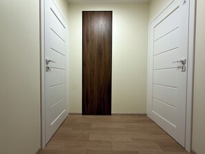 A hallway with two white doors and a wooden door at the end. - Madalińskiego Modern Studio 8A (Wrocław)