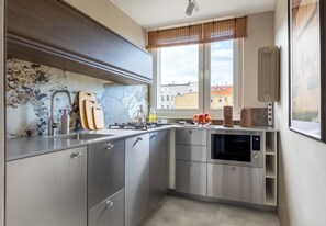 Una cocina moderna con electrodomésticos de acero inoxidable, un ventanal con vistas a edificios y una tabla de cortar de madera.