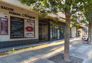 A salon with a large advertisement for cosmetic services, a tree in front, and a parked car on the sidewalk.