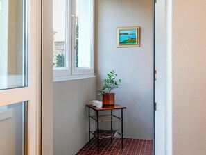 Un pasillo con una ventana, una planta en maceta, un cuadro enmarcado y una estantería metálica con un libro.