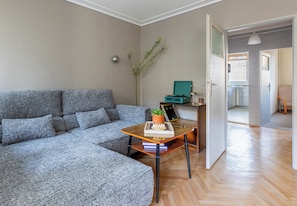 Uma sala de estar moderna com um sofá cinzento, uma mesa de centro de vidro e uma pequena planta.